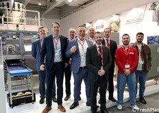 Foto di gruppo allo stand IMA. L'azienda offre soluzioni di confezionamento per l'ortofrutta con macchine orizzontali, verticali e flow wrapper. Sistemi di pesatura e conteggio gestiscono prodotti freschi e surgelati, garantendo integrità e sicurezza.